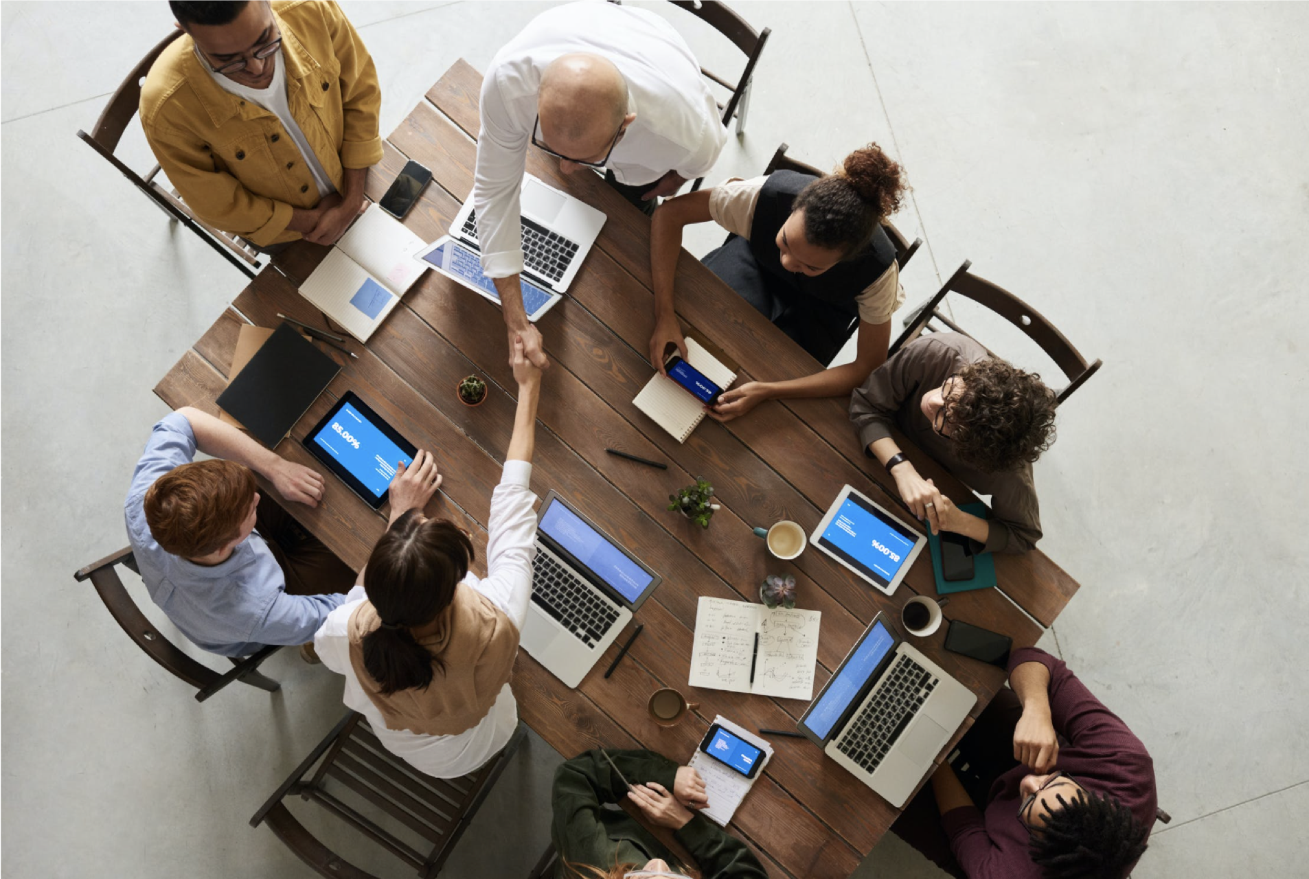 team meeting with computers gathered around a rectangular wooden table